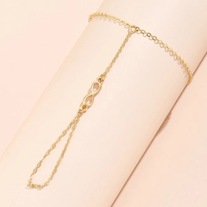Detailed view of a golden infinity symbol hand chain bracelet on a neutral display stand