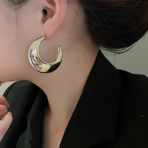 Close-up of a large silver C-shaped polished metal earring worn by a model in a black blazer