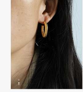 Close-up of a model wearing textured golden square hoop earrings with a spiral design