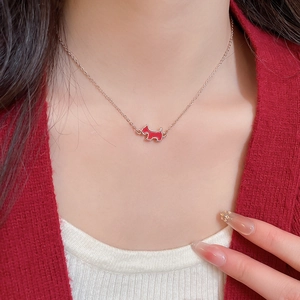 Close-up of a red enamel puppy pendant on a gold chain necklace worn by a female model