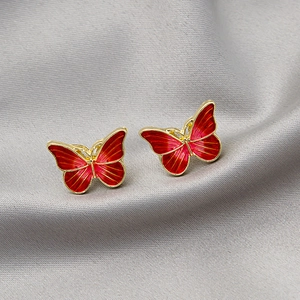 Macro shot of red butterfly earrings with gold metal frame on grey silk fabric background