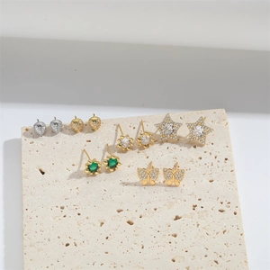 Close-up of gold and silver stud earrings in star, butterfly, and flower shapes on stone