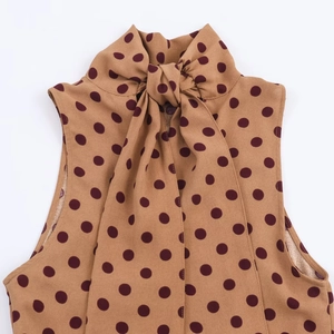 Detailed view of brown sleeveless polka dot top with a high neckline and bow tie decoration