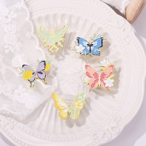 Five colorful enamel butterfly brooches with floral patterns on a white vintage plate