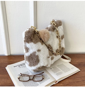 Detail of plush cow print tote bag with thick gold chain strap and fluffy charm