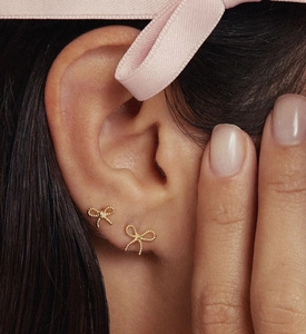 Macro view of gold bow knot stud earrings featuring a delicate woven texture on earlobe