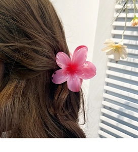 Pink resin plumeria flower hair claw clip securing a bun on brown wavy hair