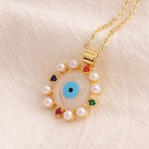 Gold evil eye necklace with colorful zircons and pearls on beige linen background