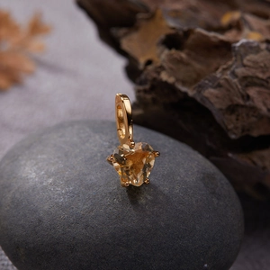 Detailed view of heart-shaped citrine gemstone pendant with golden clasp on a pebble