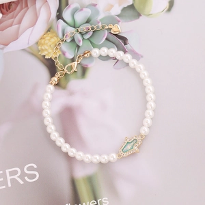 Detail of Hamsa Hand pearl bracelet with green stones and elegant golden heart charm