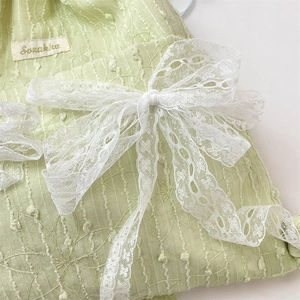 Detail of light green floral lace drawstring bag featuring a large white bow decoration