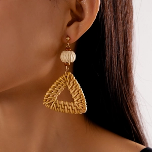 Close-up of bohemian woven triangular earrings on model featuring natural rattan texture