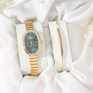 Elegant gold oval quartz watch with green dial and matching bracelet set on silk