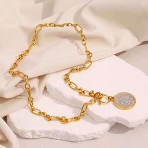 Detailed macro of gold chain necklace with silver Mexican coin pendant on stone