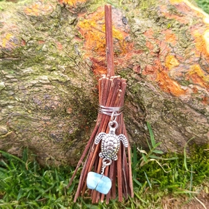 Mini witch broom charm with silver turtle pendant and blue gemstone on mossy background