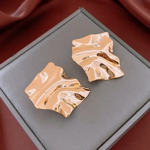 Detail view of irregular square gold-plated stud earrings on a gray jewelry box