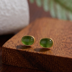 Macro shot of oval green jasper stud earrings with gold plating on a natural wood block