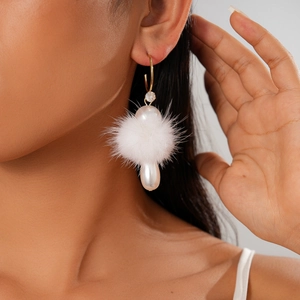 Close-up of elegant C-shaped gold earring with white faux pearl and plush pom pom