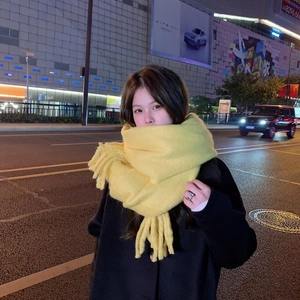 Detail of soft yellow mohair scarf with fringe trim worn by a model in a night street setting