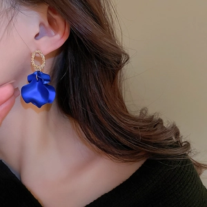 Model wearing gold textured rings with royal blue petal-shaped drop earrings