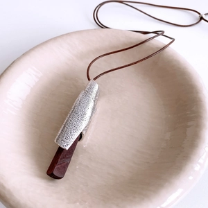 Detailed view of long wood pendant with antique silver metal casing on woven cord