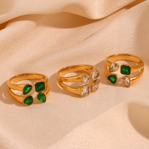 Detailed shot of three gold rings with green and clear zircon stones on beige silk