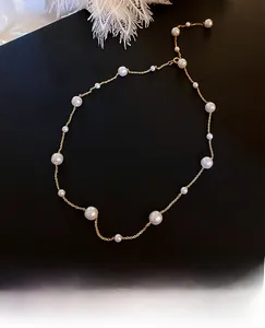 Detail of minimalist gold pearl necklace with various sizes on a textured black background