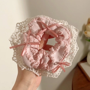 Detail van roze geplooide scrunchie met witte kantrand en kleine strikjes van lint