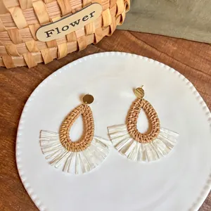 Detail of bohemian drop-shaped raffia earrings with fan fringe on a decorative tray