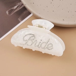 Macro shot of white pearlescent hair claw clip with crystal rhinestones spelling Bride