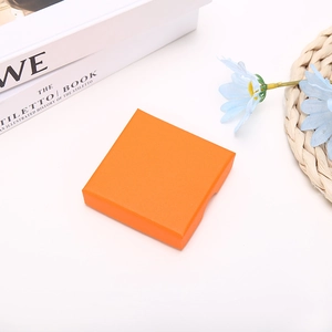Close-up of bright orange square jewelry gift box with textured surface on a white desk