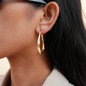 Macro shot of geometric twisted teardrop earrings with a glossy golden finish on a model