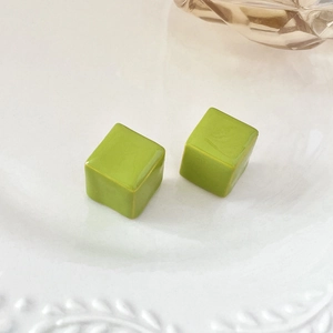 Macro detail of cube-shaped lime green stud earrings with polished ceramic finish