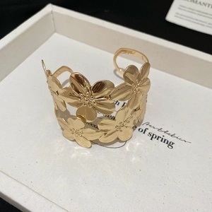 Detailed close-up of a gold cuff bracelet featuring layered metal floral patterns