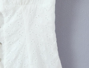 Macro view of white hollowed-out floral embroidery details on cotton blend fabric