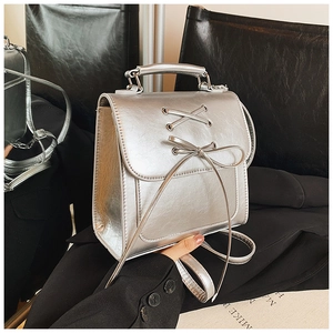 Close-up of shiny silver PU leather backpack with decorative lace-up bow and metal texture