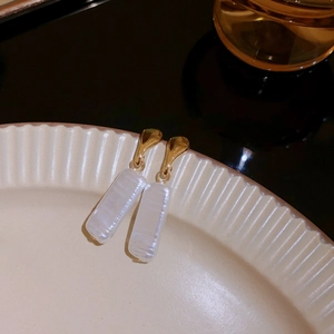 Detail of golden irregular droplet earrings with iridescent shell pendants on ceramic tray
