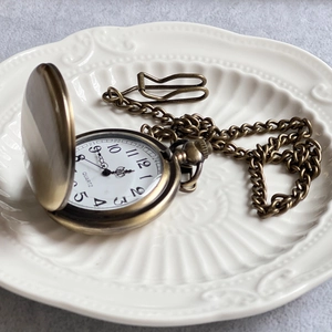Close-up of vintage bronze Alice pocket watch with chain on embossed ceramic plate