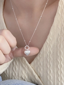 Elegant silver heart necklace with radial texture on a beaded chain worn by a model