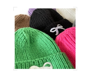 Close-up of thick knit beanies showing colorful yarn textures and bow embroidery