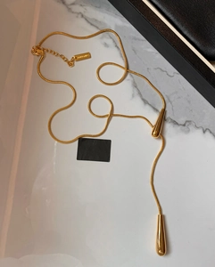 Detailed close-up of golden teardrop pendants on a snake chain necklace with brand tag