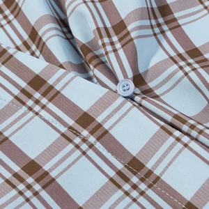 Détail d'une chemise en popeline à carreaux bleu et marron avec bouton transparent