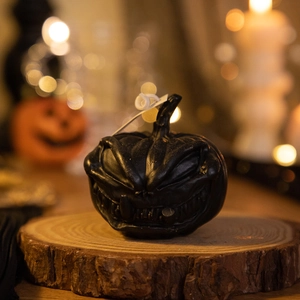 Detailed view of a black pumpkin candle on a wooden stand with festive warm lighting