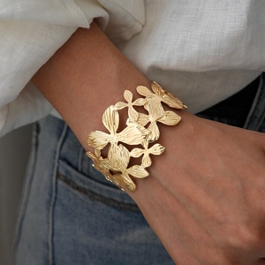 Close-up of golden hollow flower cuff bracelet with brushed metal texture and floral design