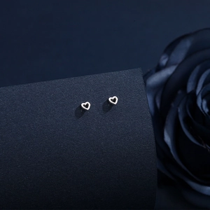 Macro shot of minimalist hollow heart silver stud earrings with a navy background