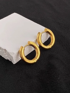 Close-up of thick gold hoop earrings on white textured stone with high-shine finish