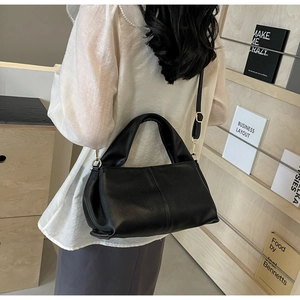 Detail of a minimalist black leather handbag with golden hardware worn as a shoulder bag
