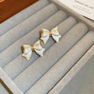 Elegant gold-plated bow stud earrings with white pearl shell inlay in jewelry tray