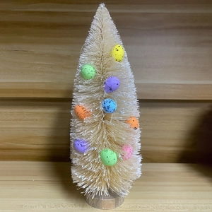 Close-up of a mini cedar Christmas tree with colorful speckled eggs on a wood base