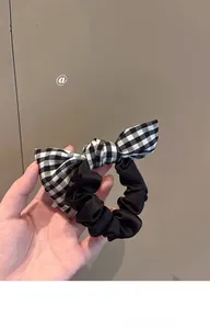 Detail of checkered bow hair tie showing black and white plaid fabric and elastic band